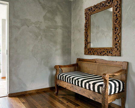 Wooden bench with striped cushion under ornate mirror in minimalist interior space.