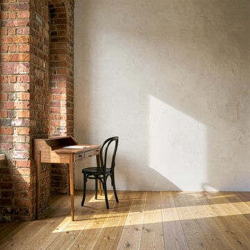 Wooden desk with chair in sunlit room beside brick wall for creative work space