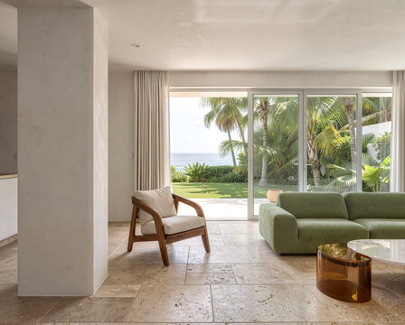 Modern living room with green sofa and wooden chair overlooking tropical ocean view through glass doors.