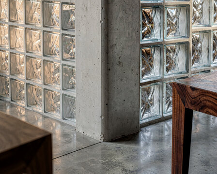 Modern interior with glass block wall, concrete pillar, wooden table on polished floor