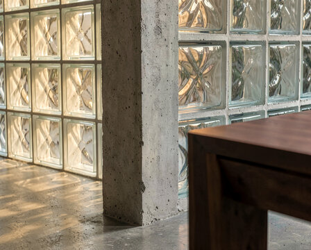 Modern interior with glass block wall, concrete pillar, wooden table, warm sunlight filtering through.
