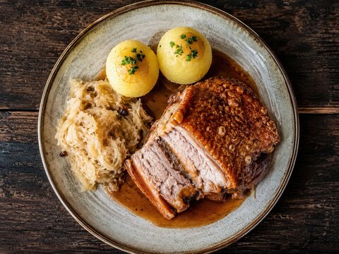 Sch&auml;ufele mit Kl&ouml;&szlig;en und Sauerkraut von oben
Fr&auml;nkisches Sch&auml;ufele mit knuspriger Kruste, Kartoffelkl&ouml;&szlig;en, Sauerkraut und So&szlig;e auf rustikalem Holztisch.
