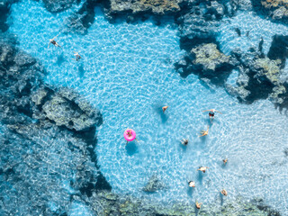 Aerial top down view of people swimming in crystal clear turquoise water of natural pool in rocks. Summer in Mallorca, Spain. Tourists relaxing with pink swim ring in Mediterranean sea. Drone view © den-belitsky