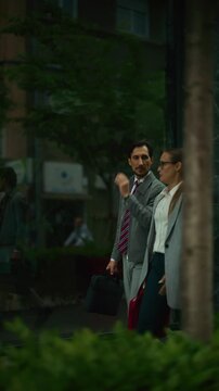 Two business professionals walk together outdoors, engaged in a focused discussion. A corporate man and woman converse while strolling past a modern office building