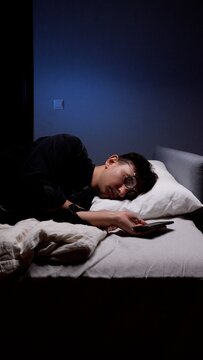 Man with glasses falling asleep in bed at night, holding a smartphone, representing digital addiction, sleep problems, screen time, and mental health issues