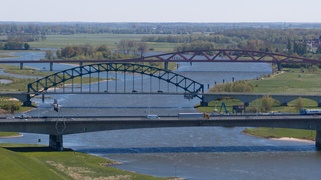 Aerial view of multiple bridges including a blue arched steel bridge and a red bridge crossing the IJssel river surrounded by green fields Zwolle, Overijssel, Netherlands.