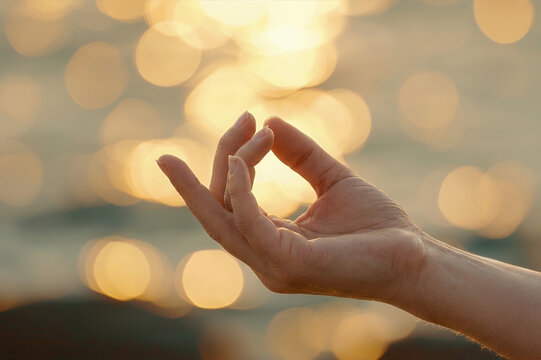 Female hand in yoga mudra on golden sunset bokeh background. Mindfulness meditation, inner balance, mental health, stress relief, holistic wellness, Pilates, meditating, calmness, fitness, sport.