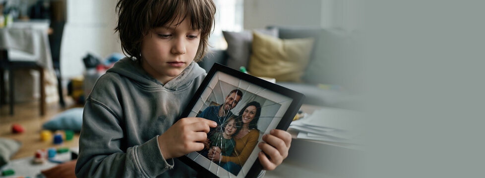 Child holding a broken picture frame showing a photo of a family. Concept of dysfunctional family and home conflict. Banner with copy space