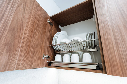 Open wooden kitchen cabinet with dish rack and white crockery