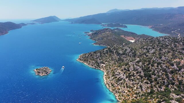 Kekova island rocky coastline and deep blue Mediterranean waters with gulets anchored in inner bay, boat underway, Antalya, Turkey
