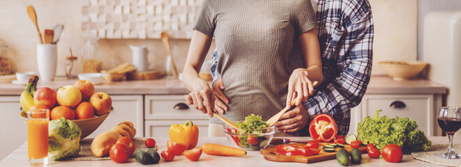 A stands close together in a kitchen preparing a meal. They chop vegetables and mix ingredients while surrounded by fruits and other food items. The atmosphere is relaxed as they enjoy cooking © Prostock-studio