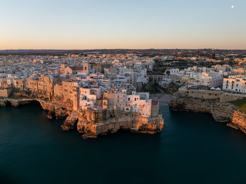 Aerial view of the historic white buildings perched on limestone cliffs above the Adriatic Sea during golden hour in Polignano a Mare, Apulia, Italy.