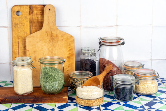 Jars of different rice with wood cutting boards on a tile surface 