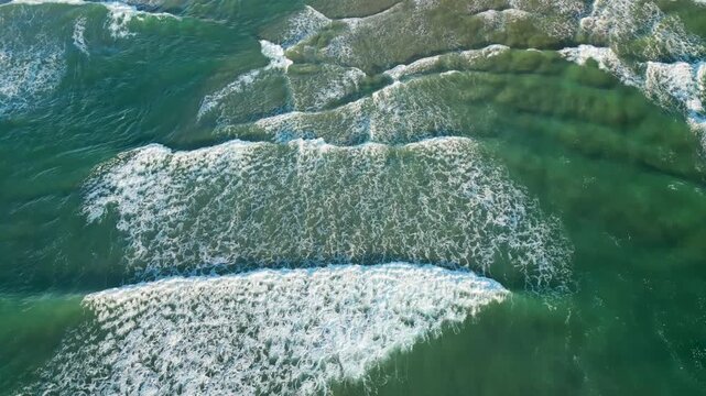 A serene aerial shot capturing emerald waves crashing onto a sandy beach shore