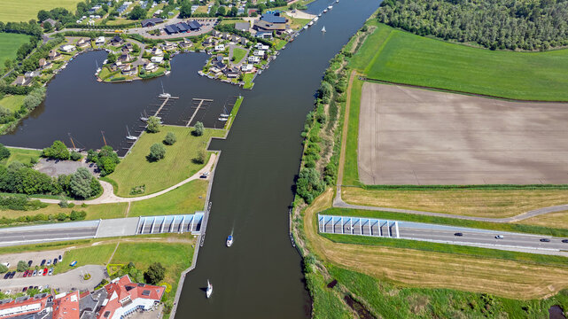 Aerial view of the Galamadammen Aqueduct crossing the Johan Friso Canal with boats sailing and cars driving underneath near the marina and fields in Koudum, Friesland, Netherlands.