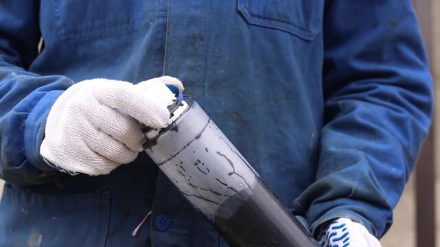 Person with plastic bottle of black pigment in hands. Master examines black paint for suitability. Woman in blue work clothes with bottle of paint, hands close-up
