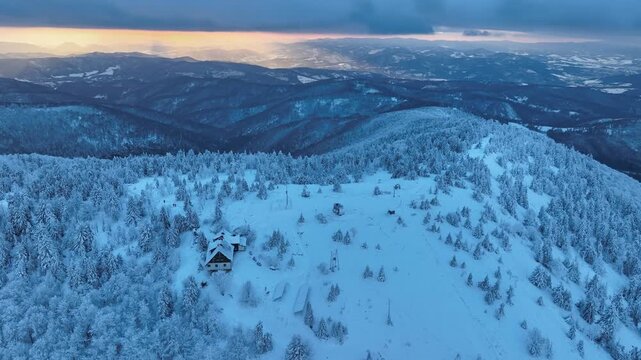 Aerial orbital shot of snow covered mountain shelter on Wielka Racza summit at winter sunset, golden hour