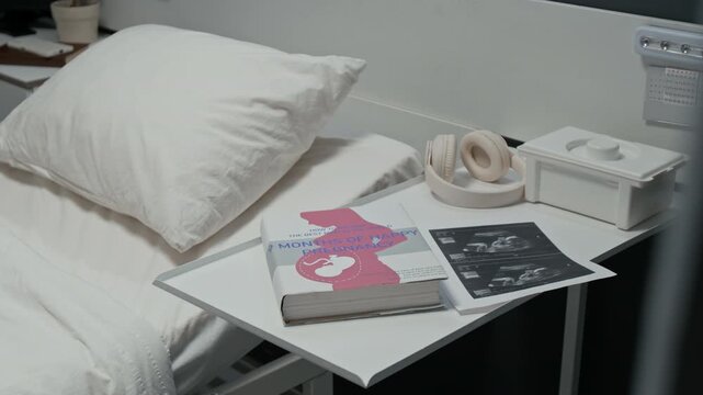 Pregnancy book,headphones,and ultrasound scans lying on bedside table next to empty hospital bed. Clip is ideal for healthcare marketing and maternity clinic promotional videos, close up