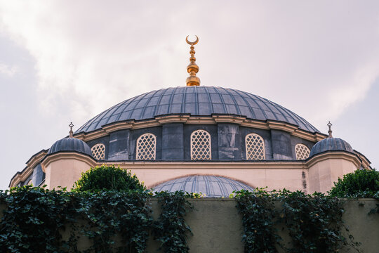 View of the Mosque of Namazgah featuring a large grey dome and golden crescent finial behind an ivy-covered wall in Tirane, Tirana County, Albania.