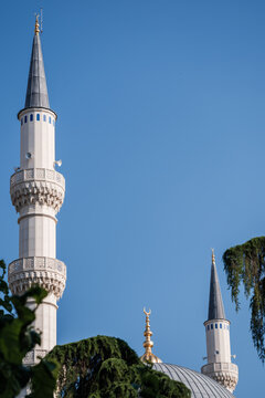View of the Mosque of Namazgah with its tall white minarets and elegant dome against a clear blue sky framed by green trees in Tirane, Tirana County, Albania.