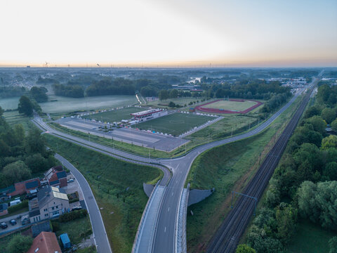 Diepenbeek, Belgium. Aerial drone view of suburban infrastructure with railway line, road intersection and sports complex in morning mist