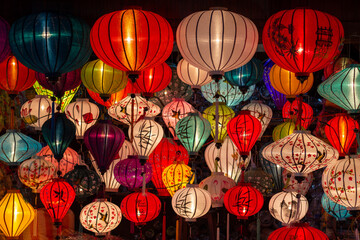 Traditional colourful Vietnamese silk lanterns illuminating a night market stall in Hoi An ancient...