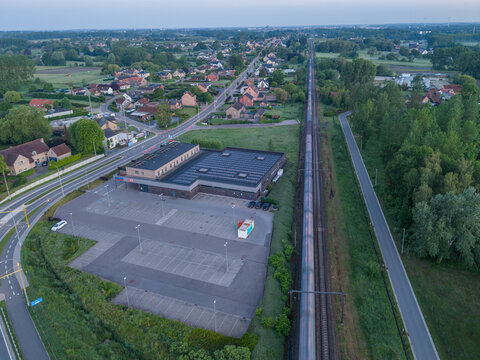 Diepenbeek, Belgium. Aerial drone view of suburban retail building with solar panels next to railway and road network at sunrise