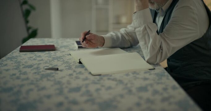 Senior man writing notes in notebook at table indoors
