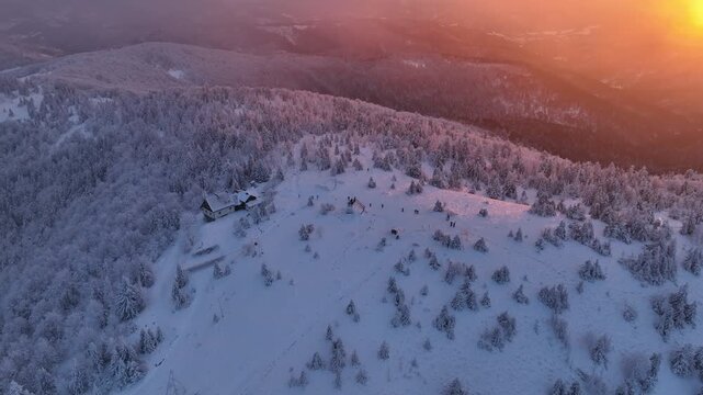 Aerial orbit and pushback from snowy mountain peak with shelter and distant hikers in low fog