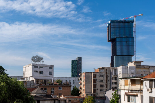 View of a modern glass skyscraper under construction with a crane overlooking residential buildings under a blue sky in Tirane, Tirana County, Albania.