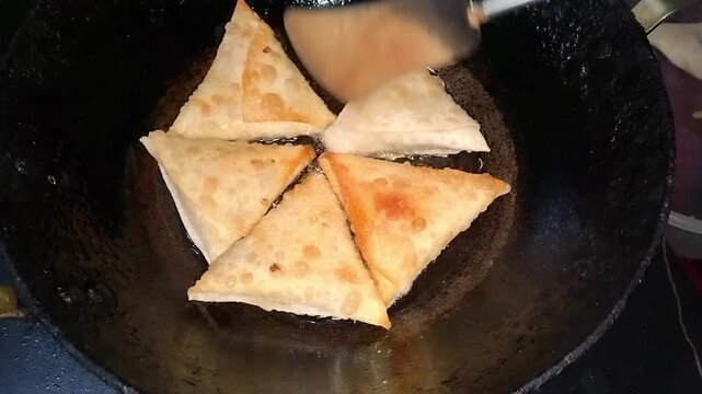 Deep frying homemade samosa triangles in hot oil in a traditional iron pan close up overhead shot of several crispy triangle shaped dough