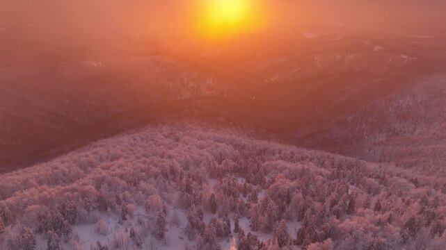 Aerial flight over winter summit towards visible sunset sun with colorful twilight clouds