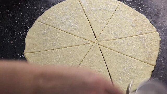 ​Close up top view of female hands rolling up cut pastry dough triangles sprinkled with sugar to shape homemade crescent rolls. Traditional baking preparation process on a dark background, step by ste