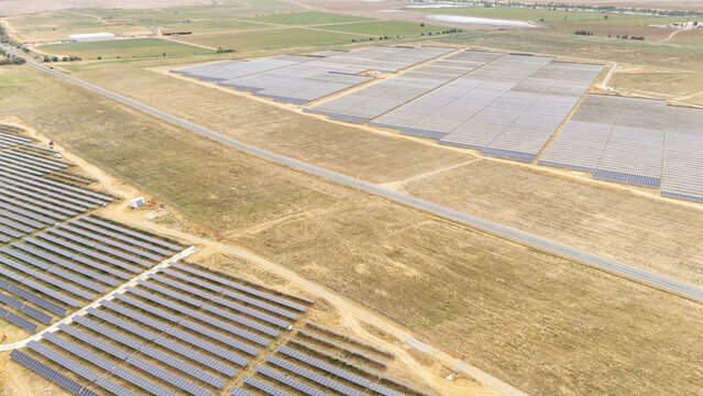 Aerial view of a large solar farm with rows of photovoltaic panels across an arid rural landscape in Andalusia, Spain.