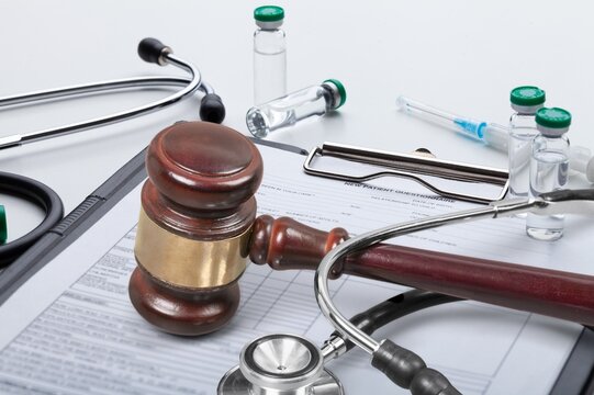 Wooden gavel and stethoscope resting on patient medical questionnaire for healthcare law and malpractice concept