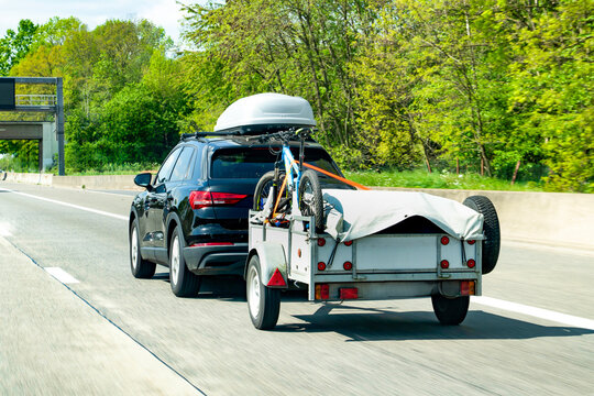 Car towing a utility trailer with a bicycle and luggage box on a highway