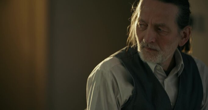Thoughtful elderly man standing in warm dim indoor light