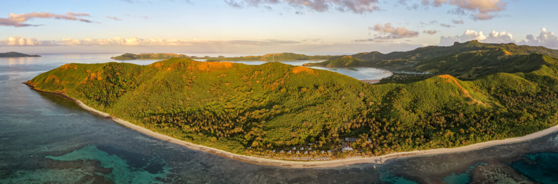 Aerial view of Naviti Island featuring lush green hills, white sandy beaches, and turquoise coral reefs under a soft sunset sky in Naviti, Western Division, Fiji.