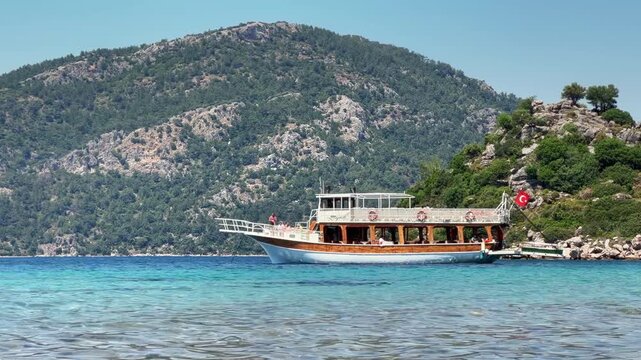 Traditional wooden excursion boat floating on the crystal clear shallow turquoise water of Cennet Bay in Selimiye, Marmaris, Turkey