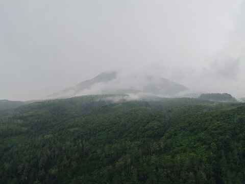 Aerial view of misty mountain peaks rising above a dense tropical forest under an overcast sky in Tawangmangu, Central Java, Indonesia.