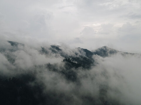 Aerial view of lush green mountain peaks shrouded in thick white clouds and mist under an overcast sky Tawangmangu, Central Java, Indonesia.