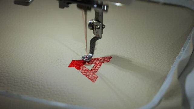 Machine embroidery of the letter "A" with red thread on light brown leather fabric.