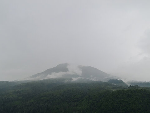 Aerial view of a mountain peak shrouded in mist and low clouds above dense green forests in Tawangmangu, Central Java, Indonesia.