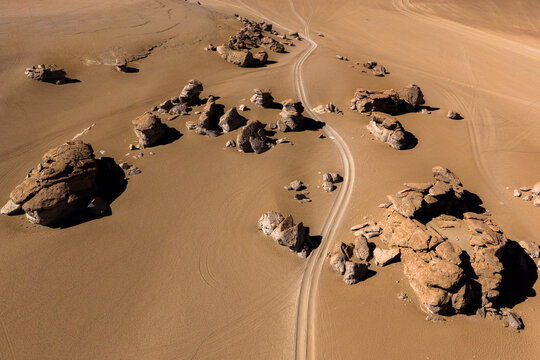 Aerial view of unique volcanic rock formations of Arbol de Piedra scattered across the arid Siloli Desert with a winding dirt road in Juntacha, Departamento de Potosi, Bolivia.