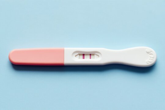 Positive pregnancy test with two pink stripes sits on light blue table. Closeup top view shows an expectant outcome. Two lines indicate a baby is coming soon. Anticipation of new life.