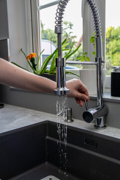 Close-up of a person turning water on or off using a modern kitchen mixer tap with a polished chrome finish and integrated pull-out spray hose. The contemporary fixture is positioned above a sink