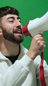 Passionate man with a beard shouting into a megaphone during a protest. Agitator making an announcement on a green screen background