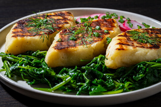Fried potato dumplings kopytka with spinach and fresh herbs. Closeup of traditional polish kopytka or ukrainian pampushky potato gnocchi served with green spinach and dill on a plate