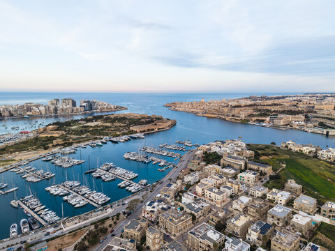 Aerial view of the Msida Marina with numerous yachts and sailboats moored near historic stone buildings and urban coastal developments in Malta.