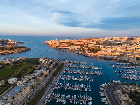 Aerial view of the Grand Harbour in Valletta with rows of yachts in the marina and historic fortifications under a soft blue sky in Malta.